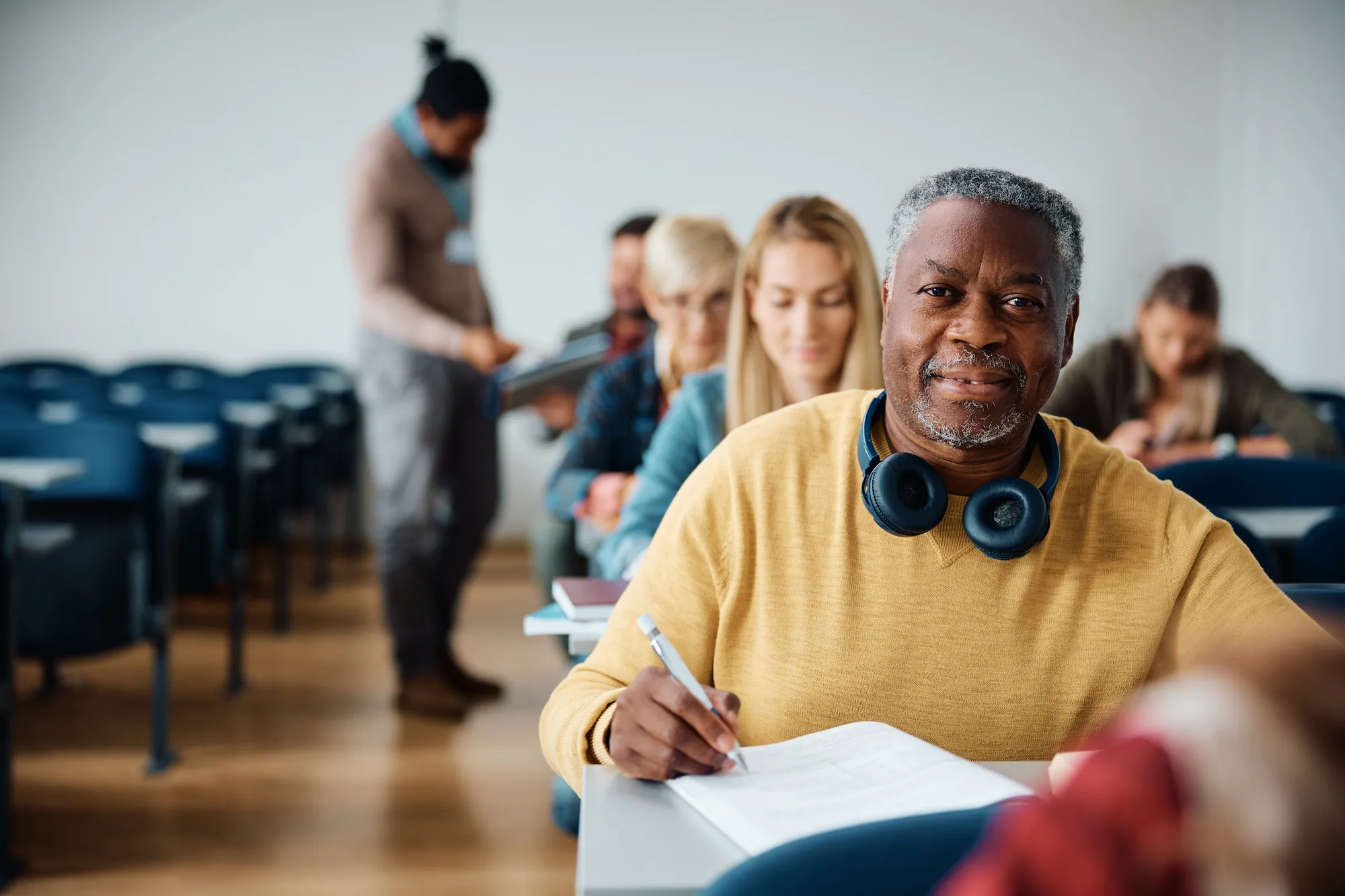 black senior student writing a test during adult educational training course and looking at camera 