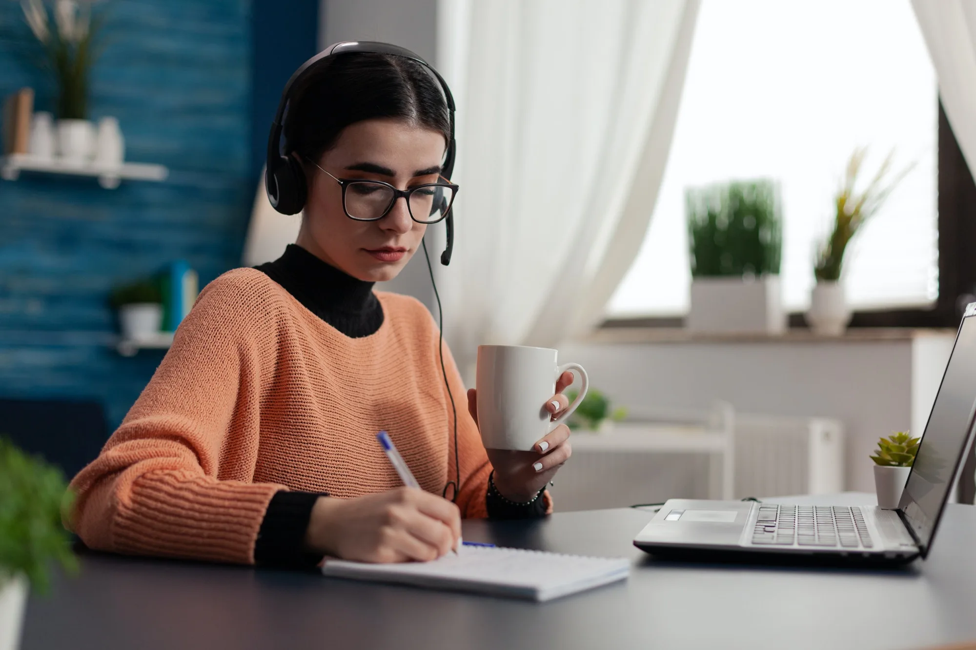 student with headphones listening to online course and taking notes