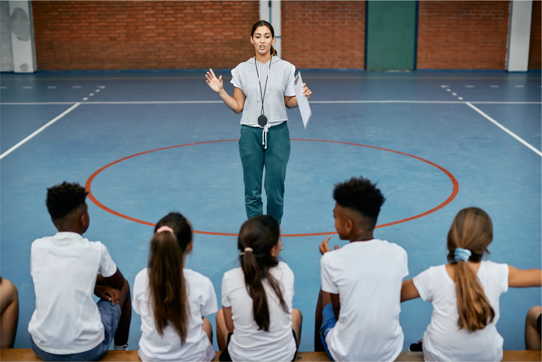 young sports teacher communicating with group of students